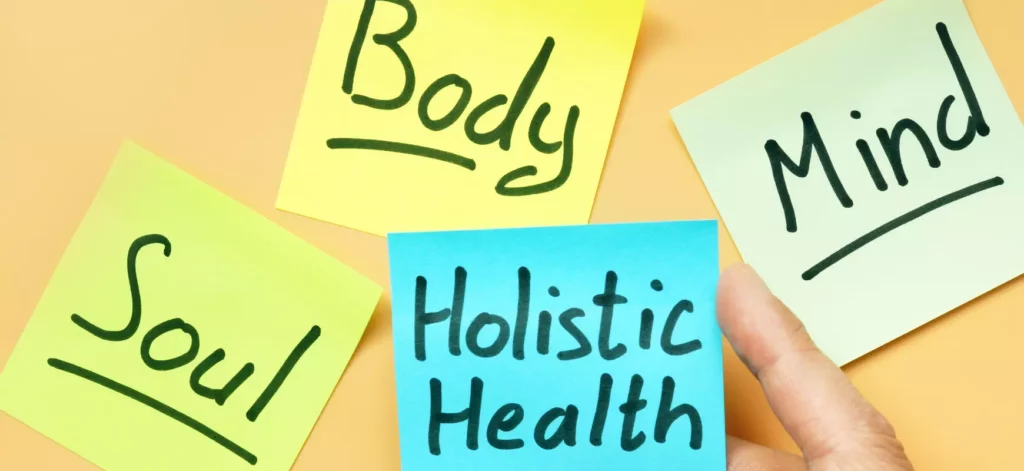 A hand holding onto sticky notes that say body and holistic health